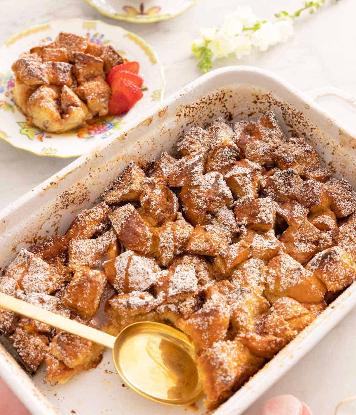A French toast casserole with a serving spoon and a serving taken out.