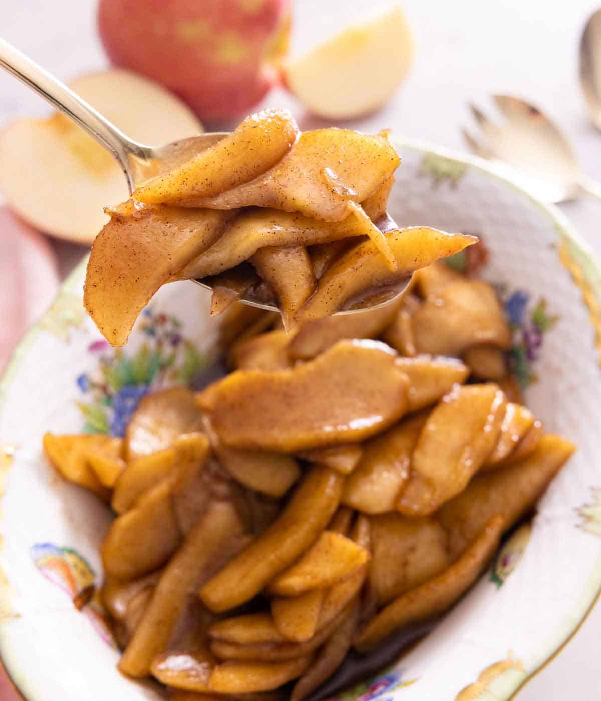 A spoon lifting a spoonful of fried apples from a plate.