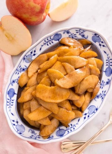 An oval platter of fried apples beside a cut apple, pink linen napkin, and two forks.