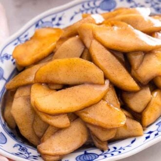 A blue and white plate of fried apples beside a pink napkin.
