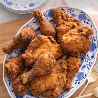 Pinterest graphic of a platter of fried chicken on a wooden board with two forks and stacks of plates beside it.
