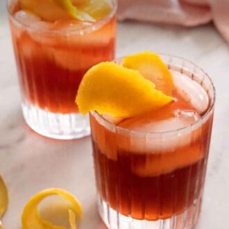 Pinterest graphic of a two glasses of Negroni with orange peel garnishes.