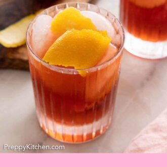 Pinterest graphic of a glass of Negroni with ice and orange peel garnish in front of a second glass and a cutting board with a peeled orange.