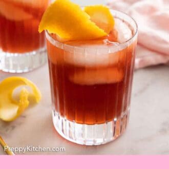 Pinterest graphic of a glass of Negroni with a linen, a second glass, and an extra orange peel in the background.