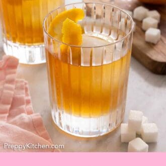Pinterest graphic of a glass of old fashioned in front of another glass with sugar cubes scattered around.