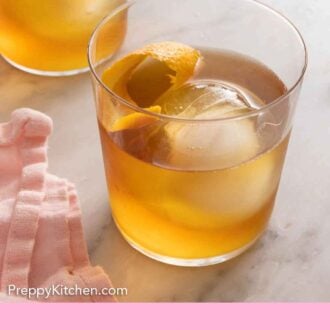 Pinterest graphic a glass of old fashioned with a circular ice cube and orange peel inside.