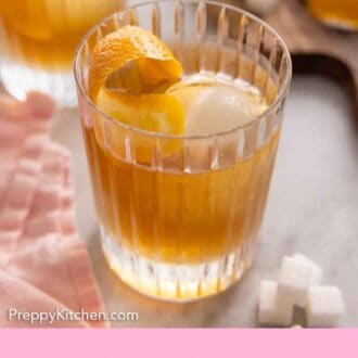 Pinterest graphic of a glass of old fashioned with a pink linen napkin on one side and scattered sugar cubes on the other.