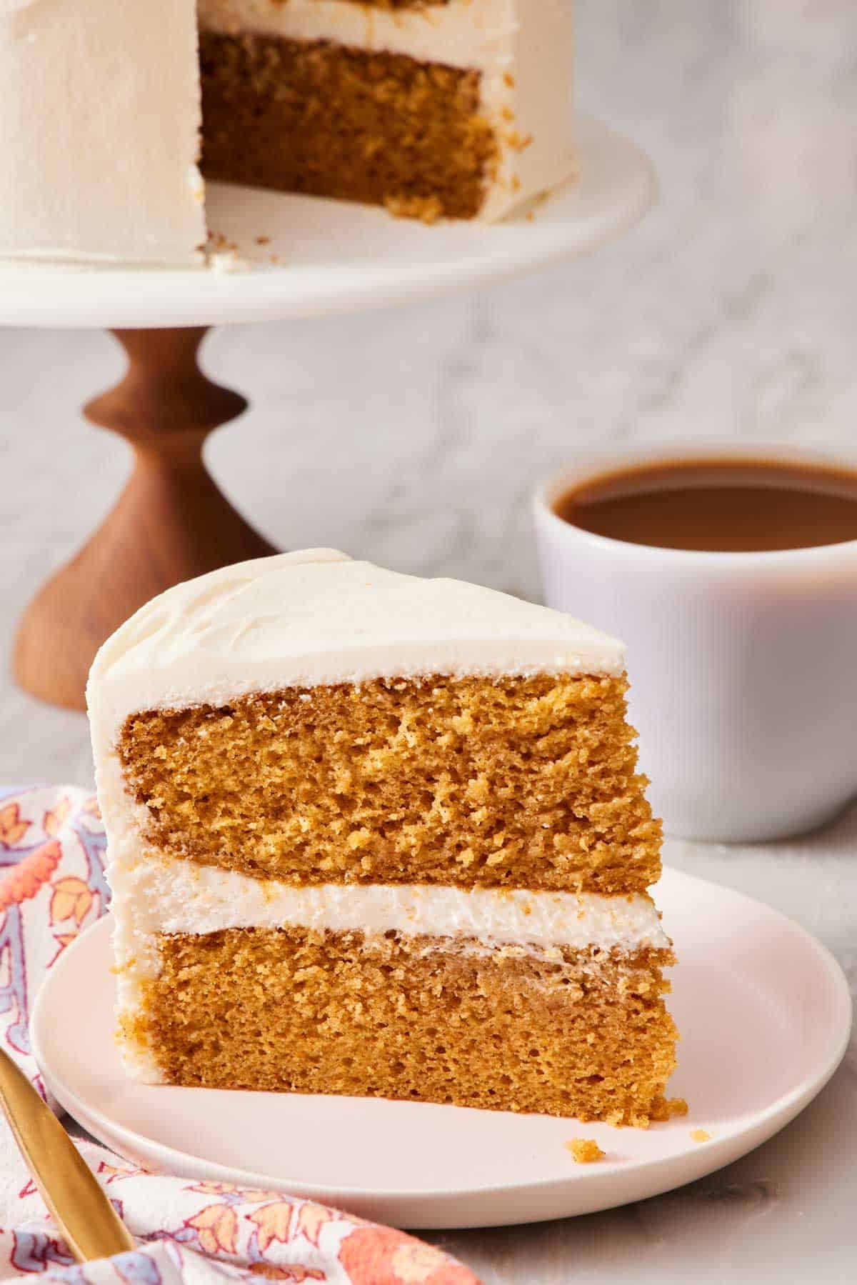 Two-layer pumpkin cake on a plate with the rest of the cake on a stand in the background.
