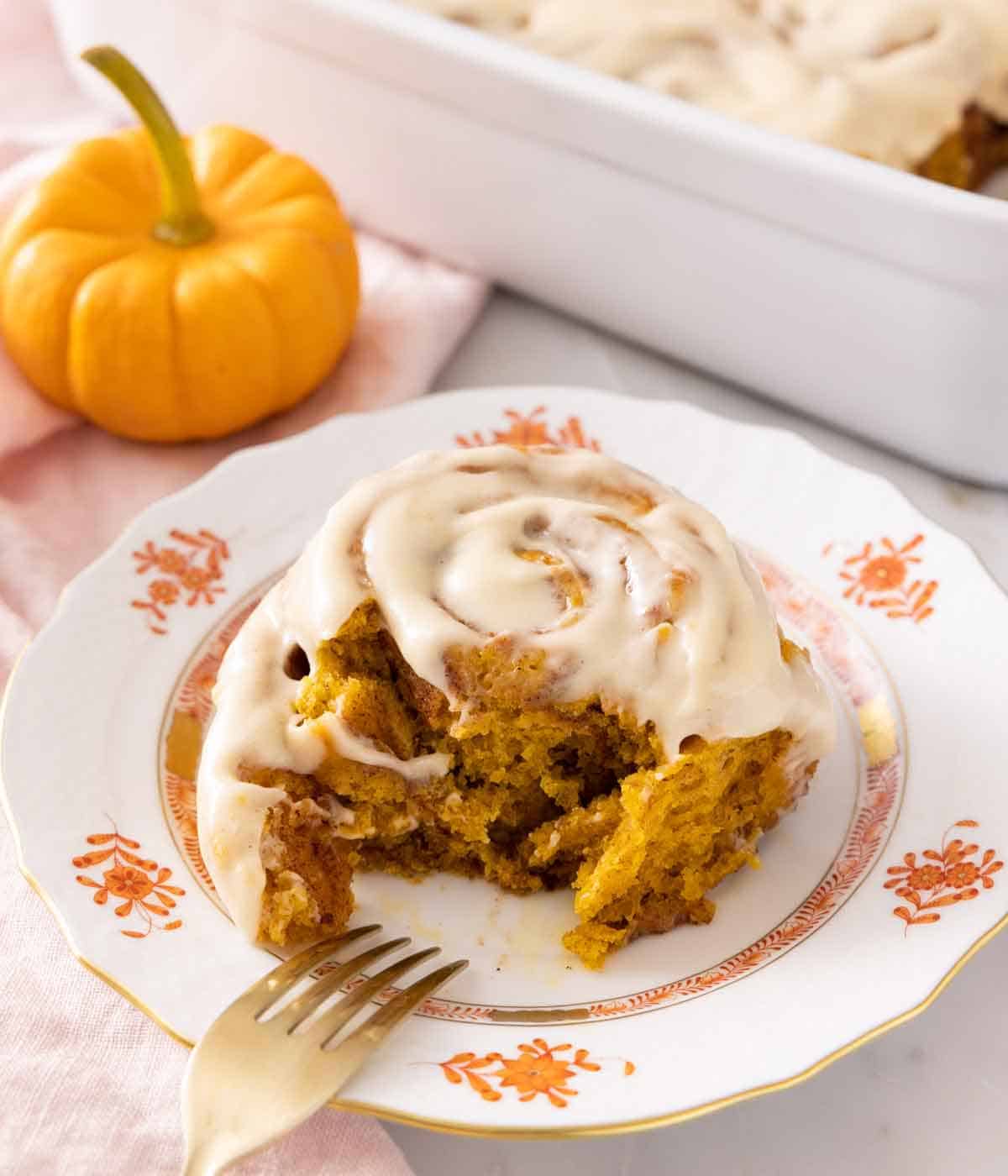 A plate with a single pumpkin cinnamon roll with a bite taken out and a fork in front of it.