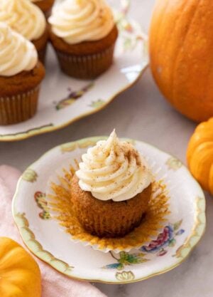 A plate with a pumpkin cupcake with cream cheese frosting on top with the cupcake liner pulled away.