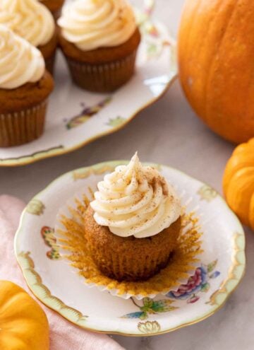 A plate with a pumpkin cupcake with cream cheese frosting on top with the cupcake liner pulled away.