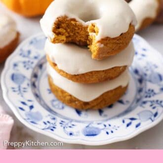 Pinterest graphic of three glazed pumpkin donuts stacked on top of each other with the top on with a bite taken out of it.