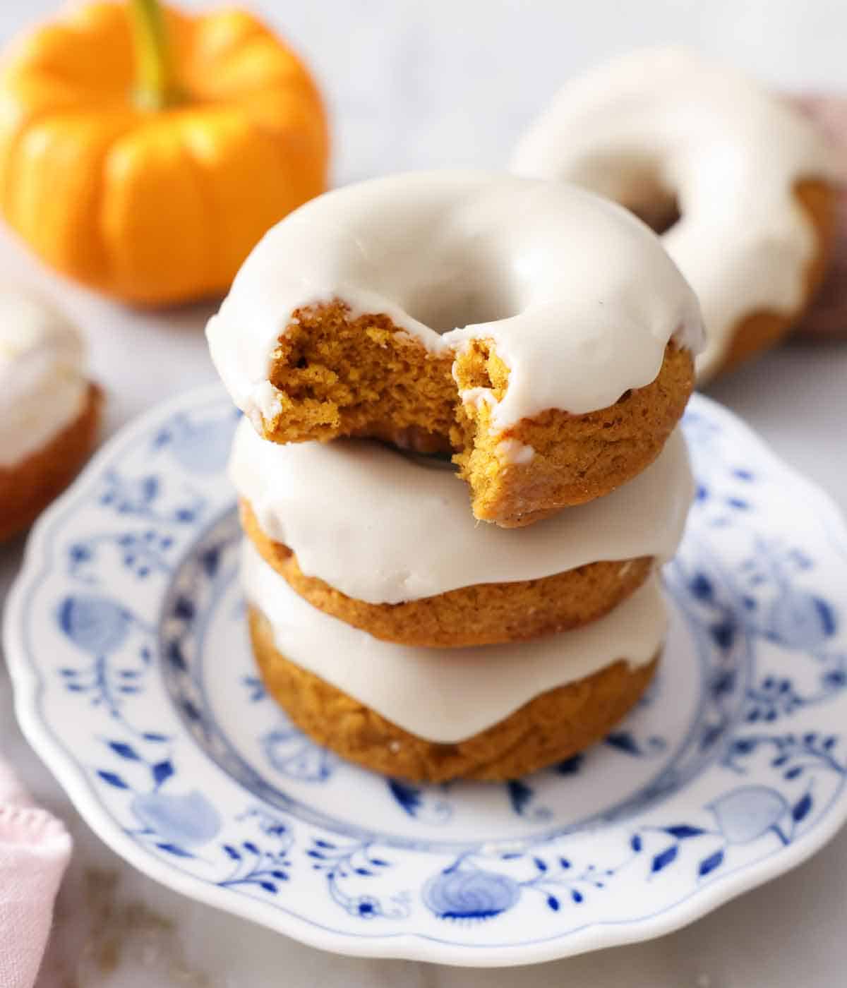 A stack of three pumpkin donuts with a bite taken out of the top donut.