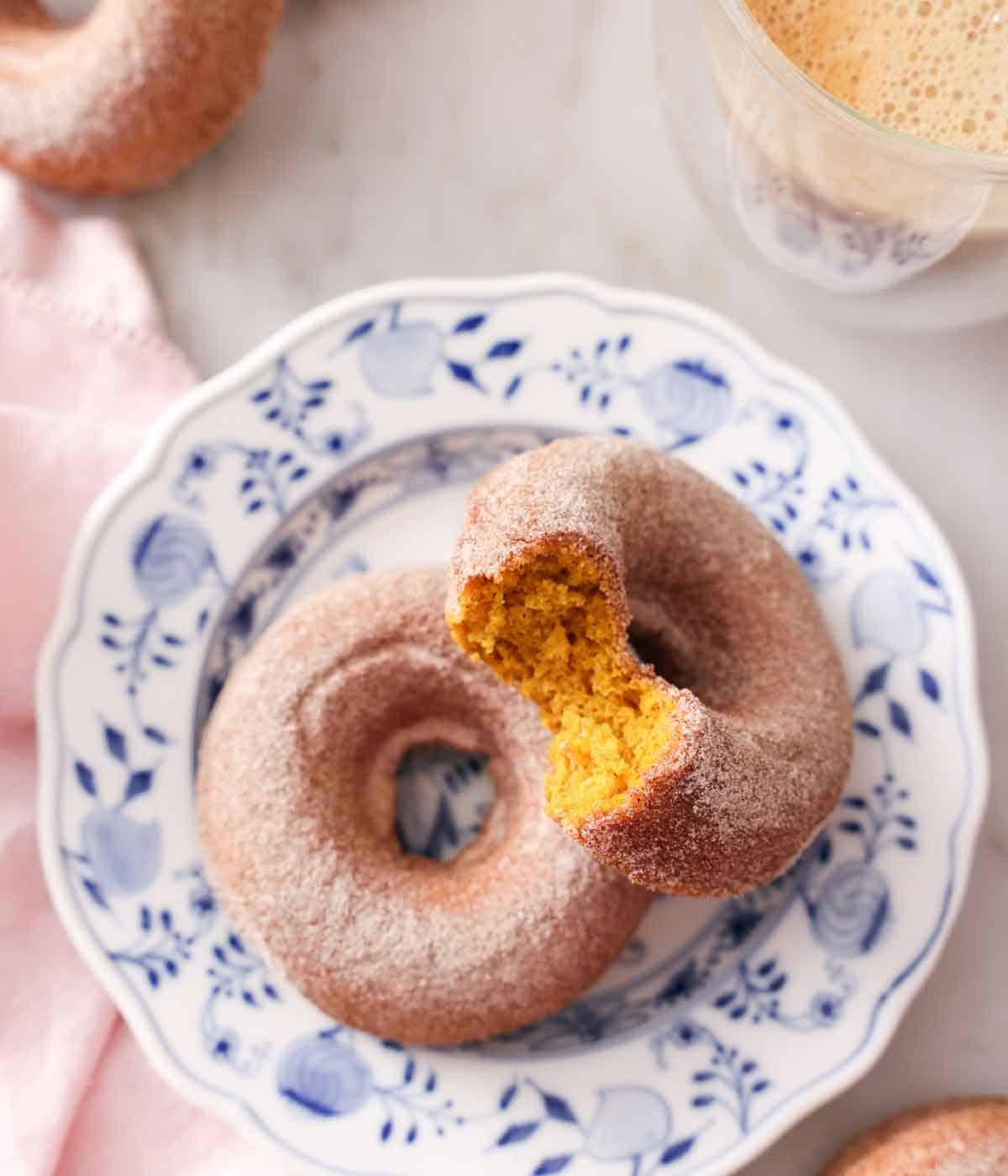 Overhead view of two pumpkin donuts with one propped on the other with a bite taken out of it.