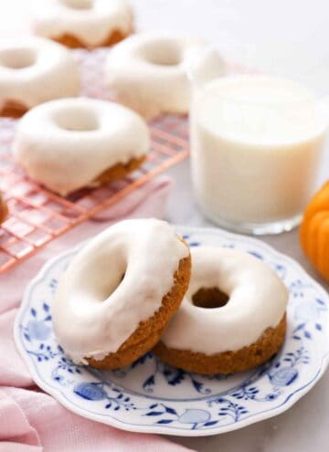 Two glazed pumpkin donuts with one propped against the other on a plate in front of a glass of milk.