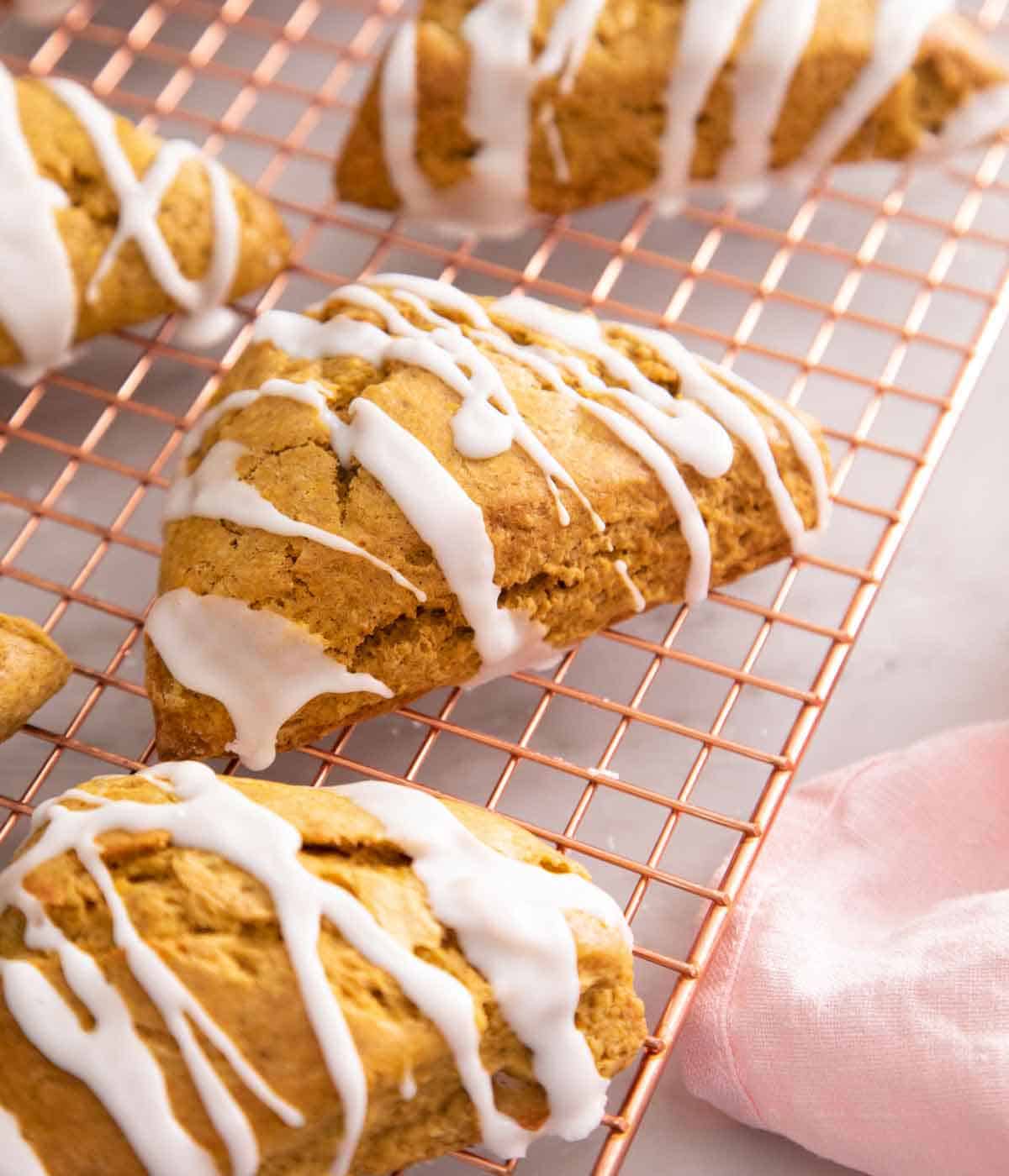 Many pumpkin scones on a wire rack with glaze drizzled on top.
