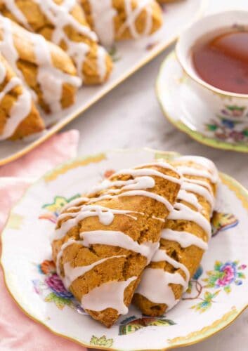 A plate with two pumpkin scones in front of a cup of tea and platter.