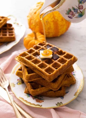 A plate with a stack of five pumpkin waffles with syrup poured on top.