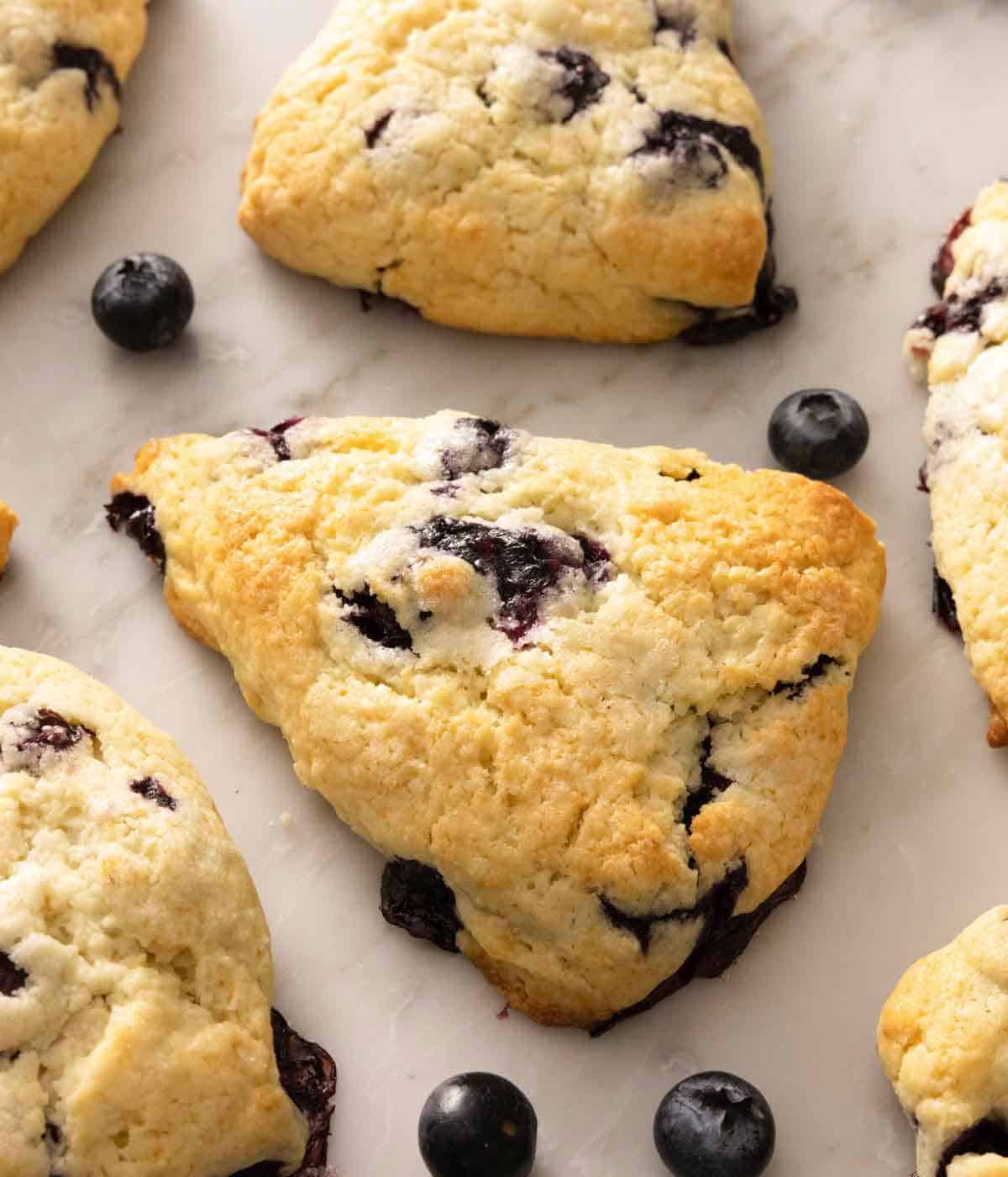 Overhead view of blueberry scones with one in focus in the middle with blueberries scattered around.