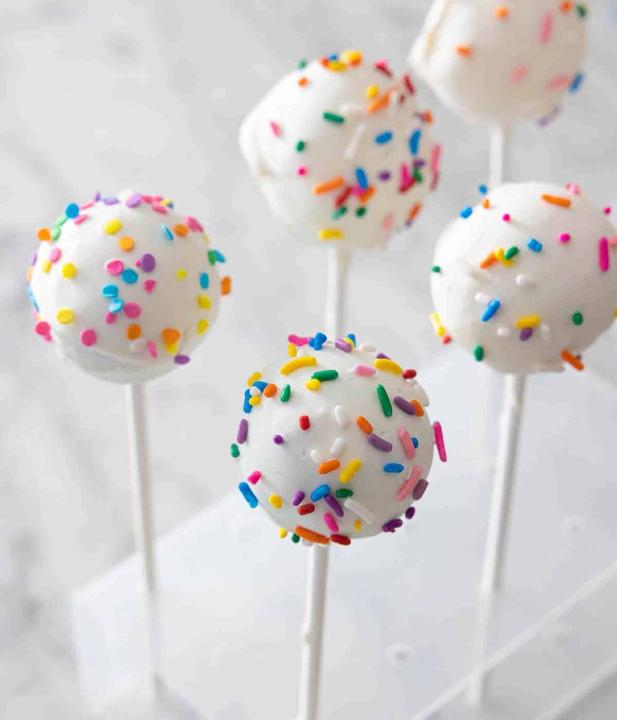 Multiple white cake pops with rainbow sprinkles.