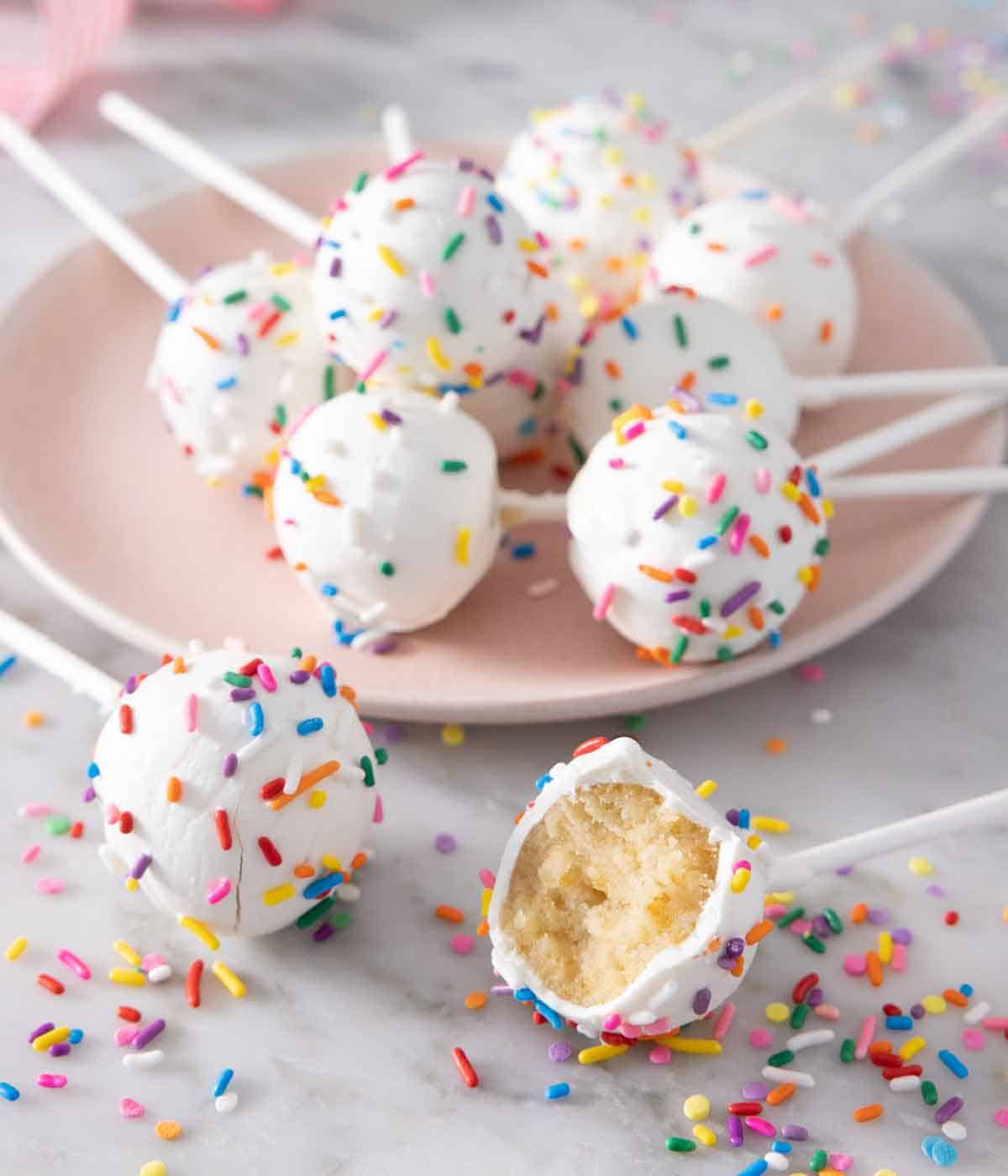 A plate of cake pops with two in front of it, one with a bite taken out.