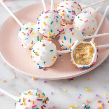 A plate with multiple cake pops on it with one with a bite taken out.