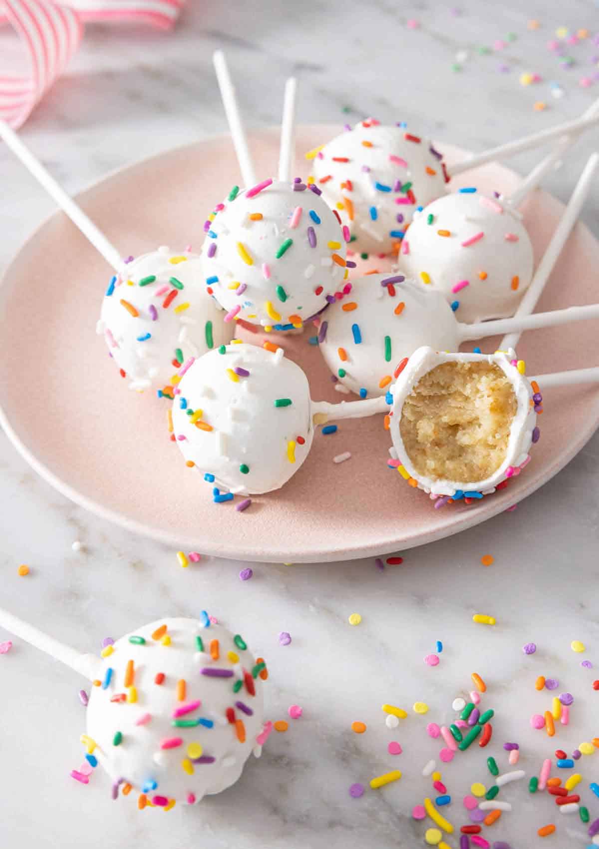 A plate with multiple cake pops on it with one with a bite taken out.