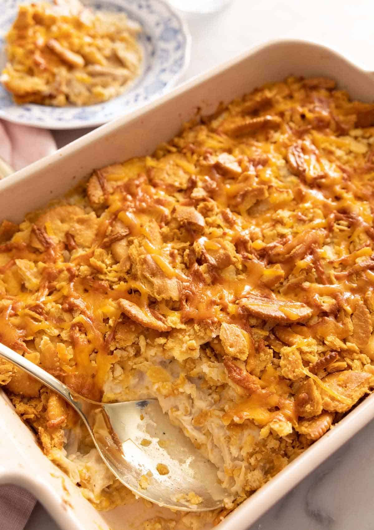 A chicken casserole with a serving removed and a spoon inside the baking dish.