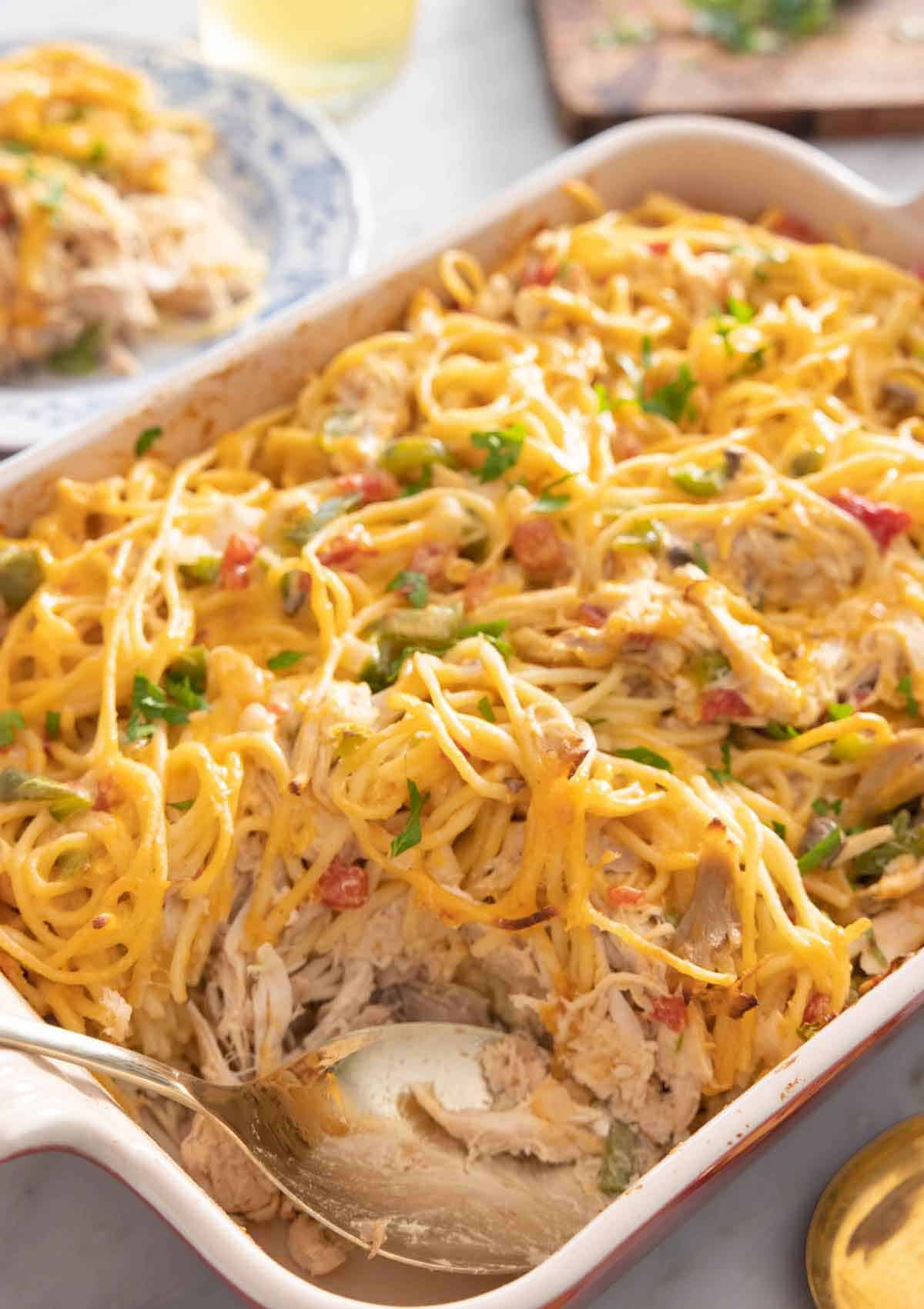 A casserole dish with chicken spaghetti and a spoon inside.
