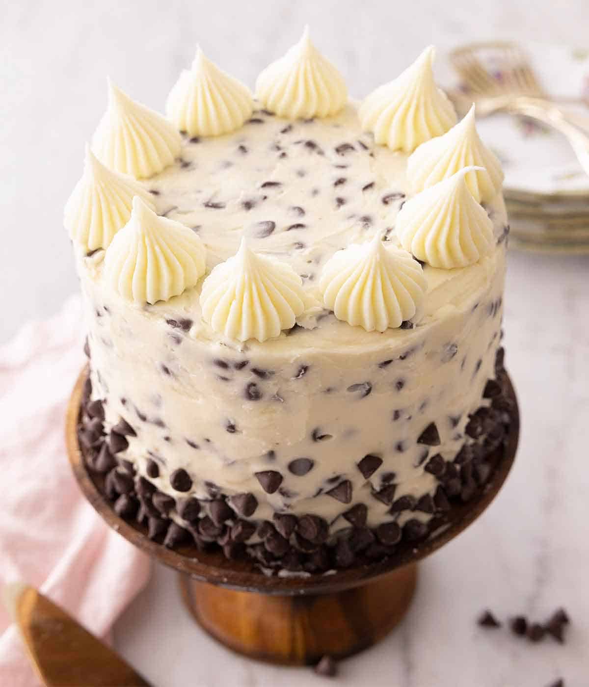 A chocolate chip cake on a brown cake stand with buttercream dollops on top.