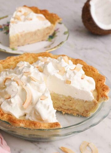 A coconut cream pie in a glass pie dish with a slice cut out.