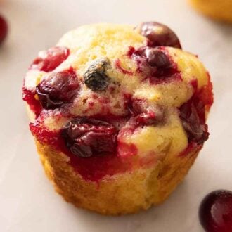 A cranberry orange muffin with some cranberries scattered.