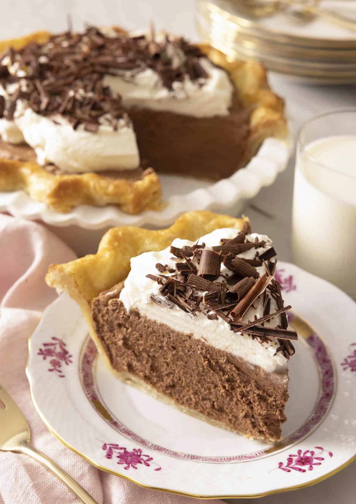 A slice of French silk pie on a plate in front of the rest of the pie.