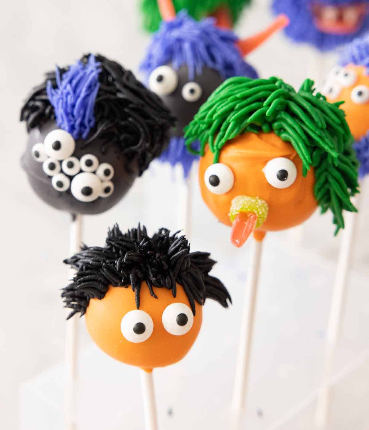 Halloween cake pops decorated as monsters with eyes and hair.