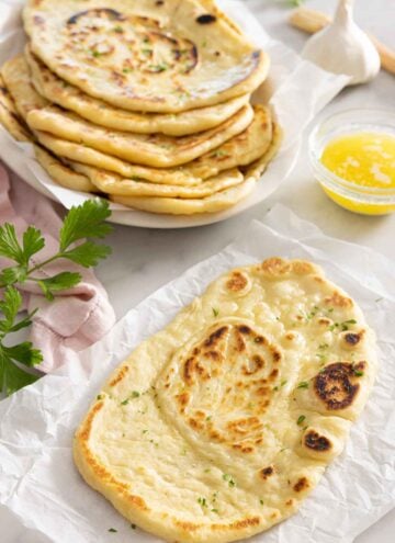 A naan bread on parchment in front of a stack of naans.