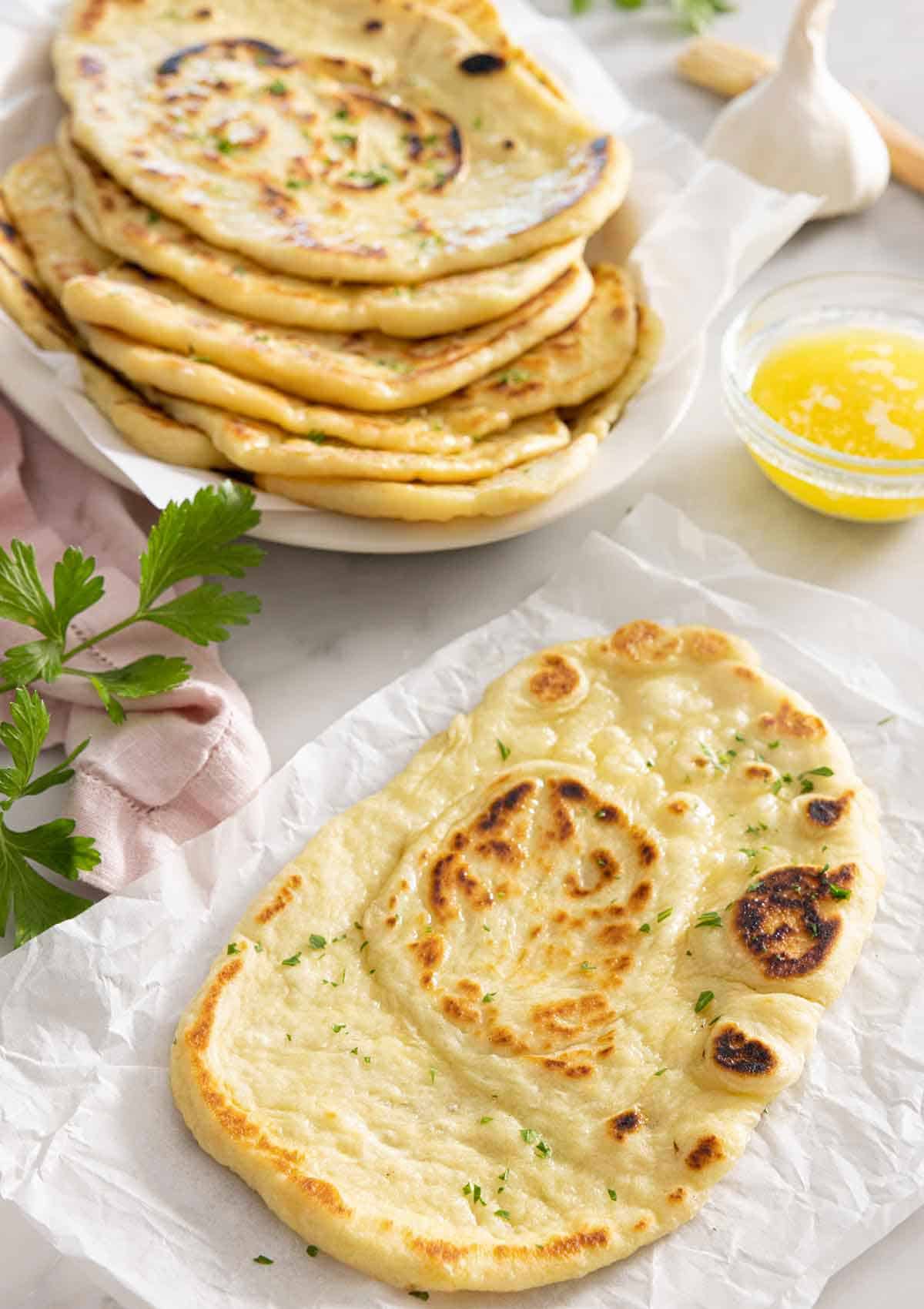 A naan bread on parchment in front of a stack of naans.