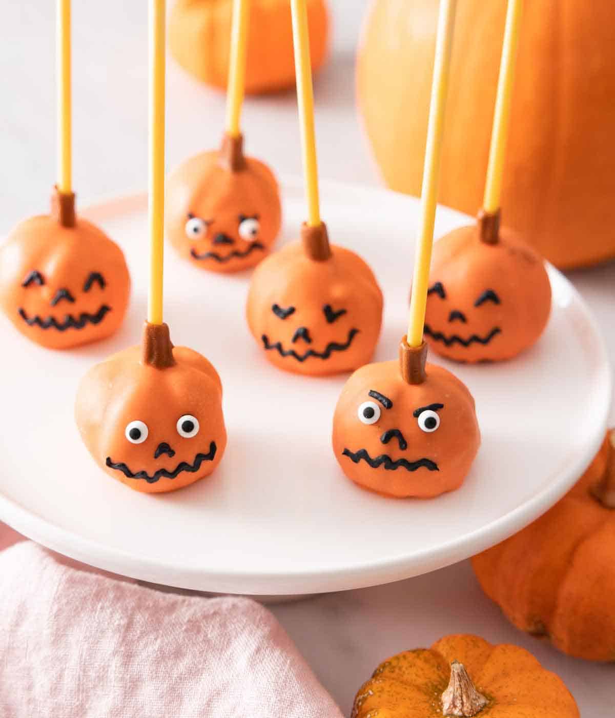 Multiple pumpkin cake pops with faces on a plate.
