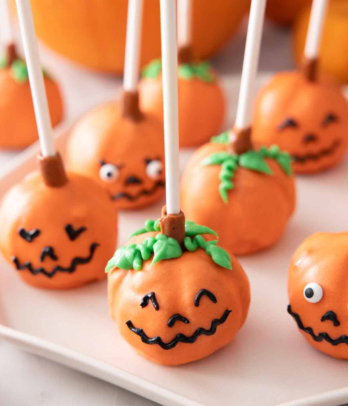 Pumpkin cake pops with smiley faces on a plate.