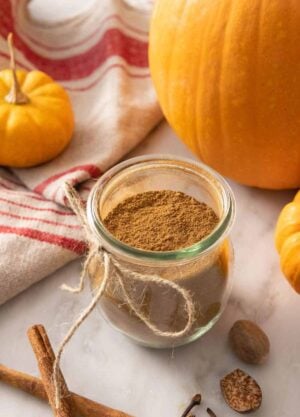 A tulip jar with pumpkin pie spice beside decorative pumpkins and scattered spices.