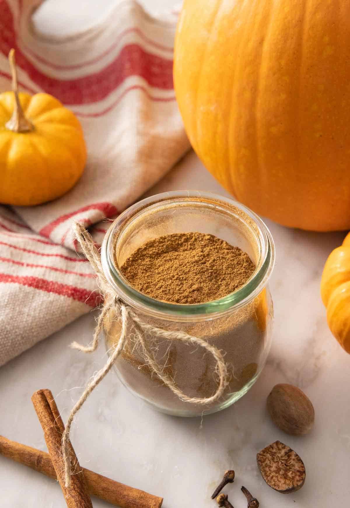 A tulip jar with pumpkin pie spice beside decorative pumpkins and scattered spices.