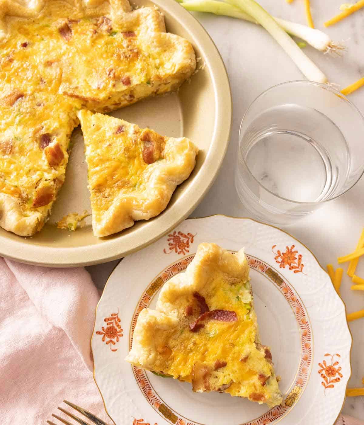 Overhead view of a slice of quiche on a plate beside a dish with the rest.