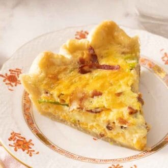 A slice of quiche on a plate beside a fork.