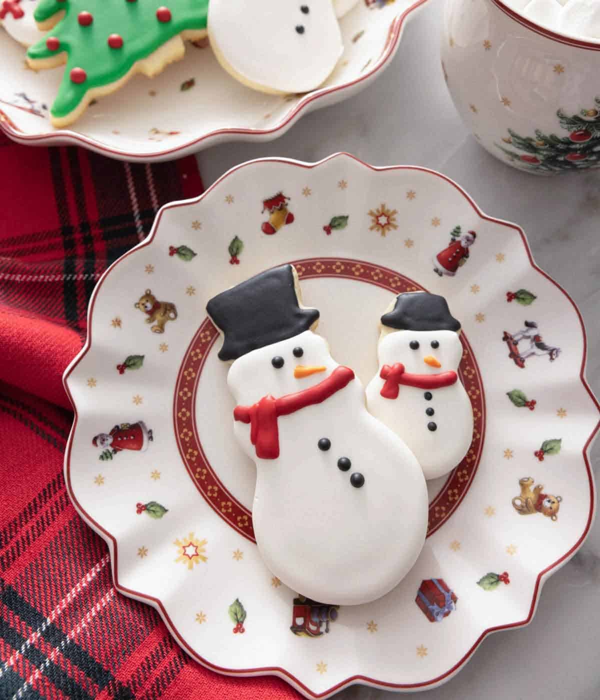 A plate with two snowman cookies decorated with royal icing.