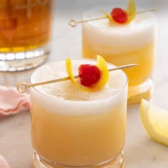 Pinterest graphic of two glasses of whiskey sours with garnish on top in front of a glass of bourbon.