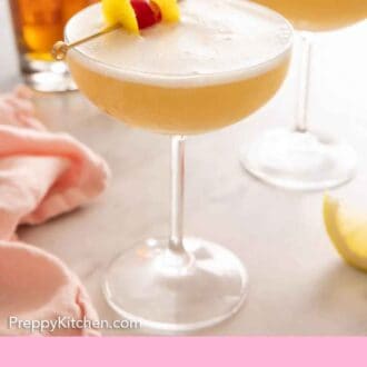 Pinterest graphic of two cocktail glasses containing whiskey sours with lemon peel and a maraschino cherry on top.