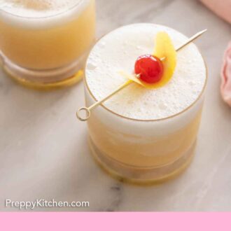 Pinterest graphic of an angled overhead view of two glasses of whiskey sour with lemon peel and cherry on top as garnish.
