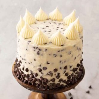 A chocolate chip cake on a cake stand with dollops of buttercream on top.