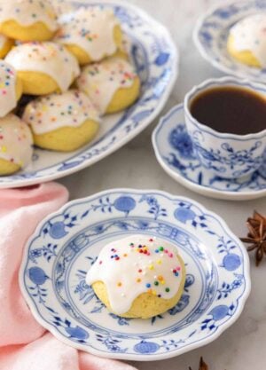 A plate with a anise cookie with sprinkles in front of a coffee.