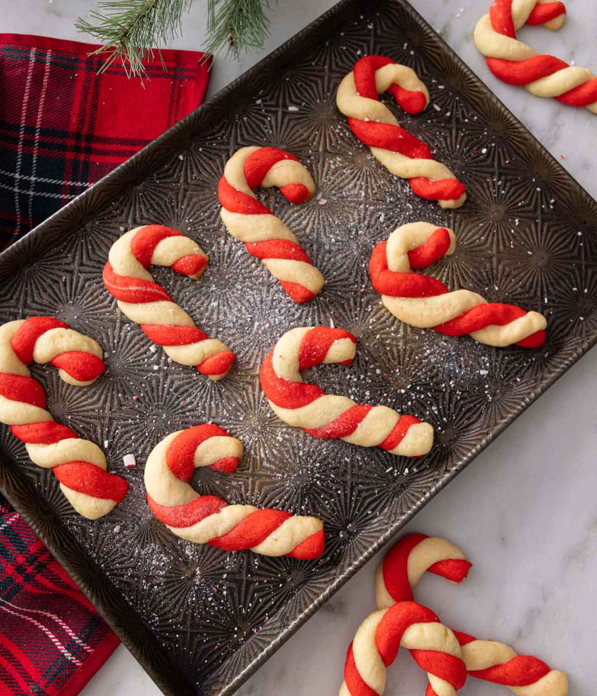 A baking tray with seven candy cane cookies with more scattered around.