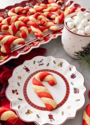 A plate with a candy cane cookie in front of a platter of them.